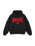 MONUMENTS raw-edge oversized hoodie in washed black cotton with red raised silicone MONUMENTS artwork, front view.