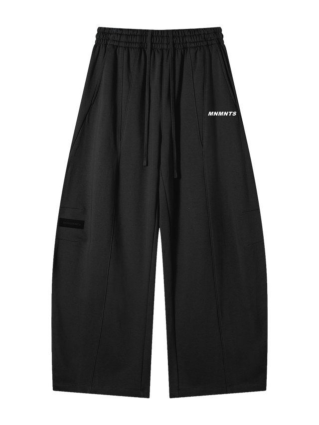 MONUMENTS structured wide-leg sweatpants in black heavyweight fleece with elastic waistband, extended drawcord and MNMNTS hip print, front view.