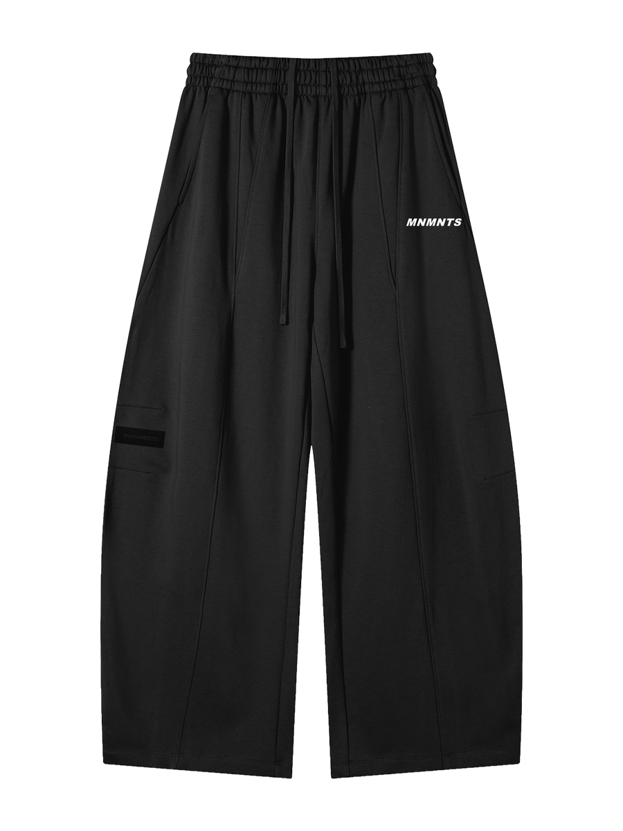 MONUMENTS structured wide-leg sweatpants in black heavyweight fleece with elastic waistband, extended drawcord and MNMNTS hip print, front view.